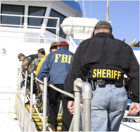 Law enforcement officers, including FBI agents and a sheriff, boarding a boat in a line on a sunny day to attend an Area Maritime Security Committee meeting.