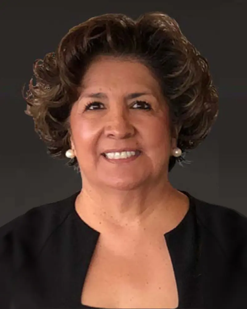 Woman with curly hair, wearing earrings and a black top, smiling against a dark background, exuding the confidence of Port Commissioners.