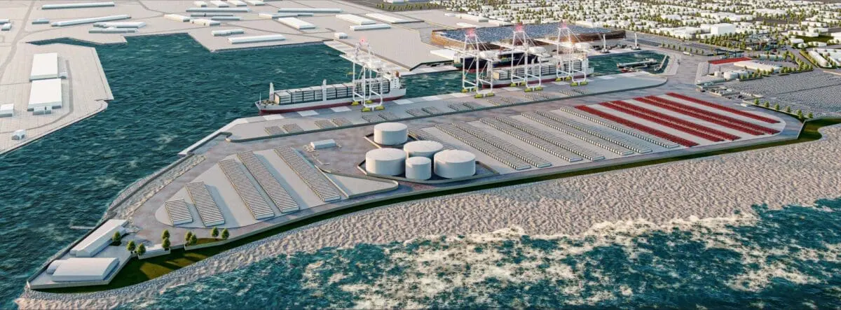 Aerial view of a coastal industrial port with multiple cranes, shipping containers, and large storage tanks, showcasing ongoing port development against an ocean backdrop.