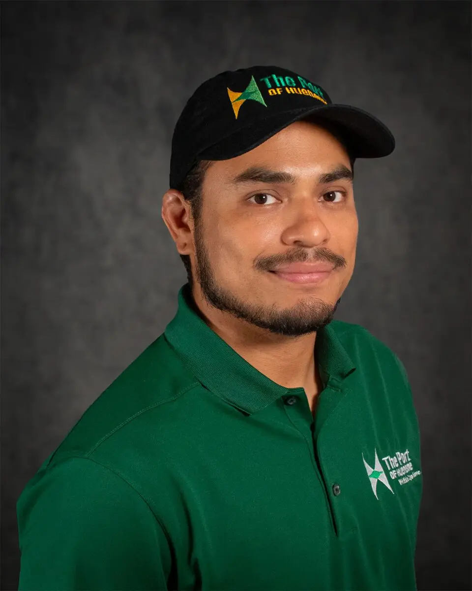 Roberto Sosa, wearing a green polo shirt and a black baseball cap with "The Port of Virginia" logo, smiles at the camera.