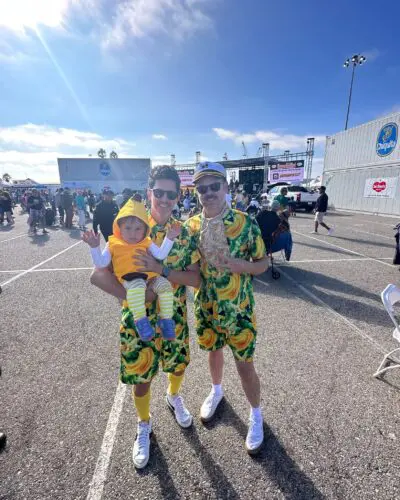 Two adults in matching banana-themed outfits and a baby dressed as a banana pose together outdoors, celebrating their unique costume choice.