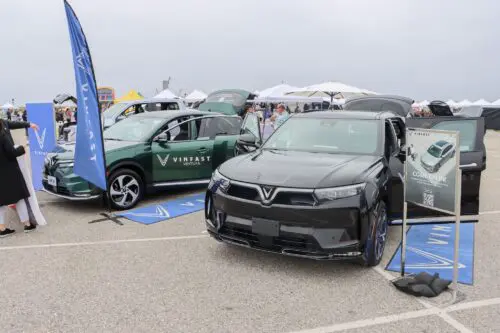 A display of two VinFast electric vehicles, one green and one black, at an outdoor event highlights the innovation in sustainable transport. Banners and informational signs about the cars are visible, showcasing California’s commitment to eco-friendly initiatives like the $3.935 Million State Grant for Port of Hueneme.