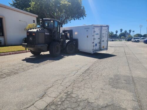 A loader vehicle transports a large white container on a sunny day in an industrial area, thanks to the $3.935 Million State Grant for Port of Hueneme as Governor Ramps Up California Port Data Partnership Program.