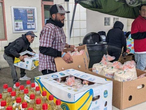 Volunteers, energized by a $3.935 million state grant for the Port of Hueneme, distribute boxes of groceries with bottled drinks and packaged foods at an outdoor event, supporting the governor's plans to enhance the California Port Data Partnership Program.