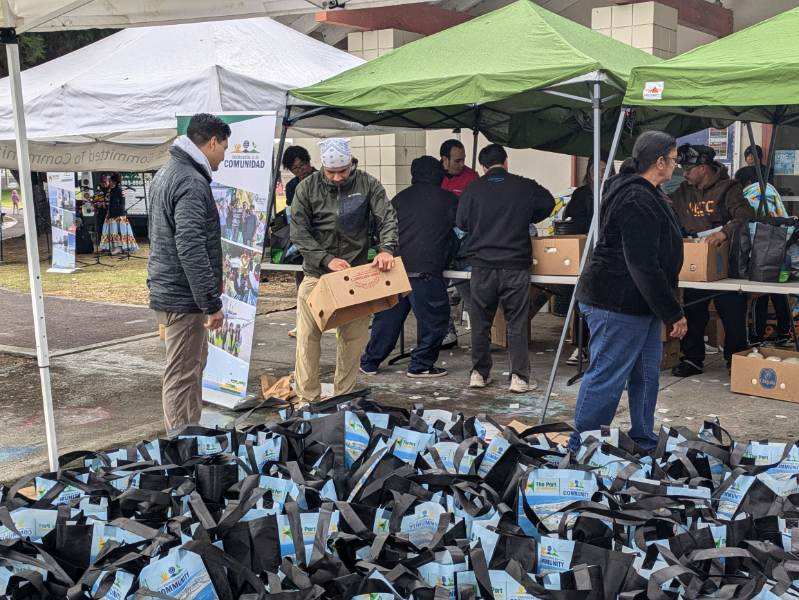 Under green tents, people distribute boxes and bags at an outdoor event, celebrating the $3.935 million state grant for Port of Hueneme as the Governor ramps up California's Port Data Partnership Program.