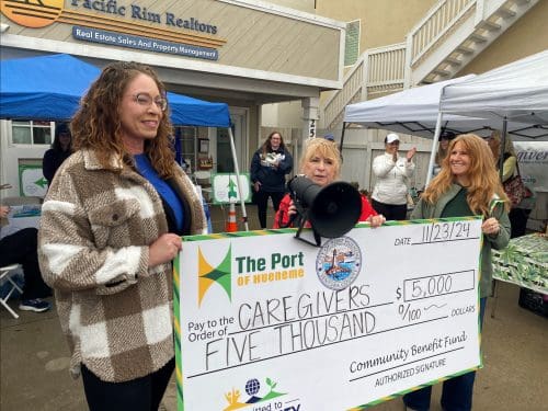 Three people hold a large ceremonial check for $5,000 addressed to caregivers, dated 11/23/24, from The Port of Hueneme at an outdoor event celebrating the port's recent $3.935 million state grant as part of Governor Newsom's initiative to enhance California's port data partnership program.