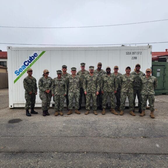 A group of uniformed military personnel stands in front of a white storage container labeled "SeaCube," showcasing the importance of the $3.935 million state grant for Port of Hueneme as Governor ramps up California's Port Data Partnership Program.