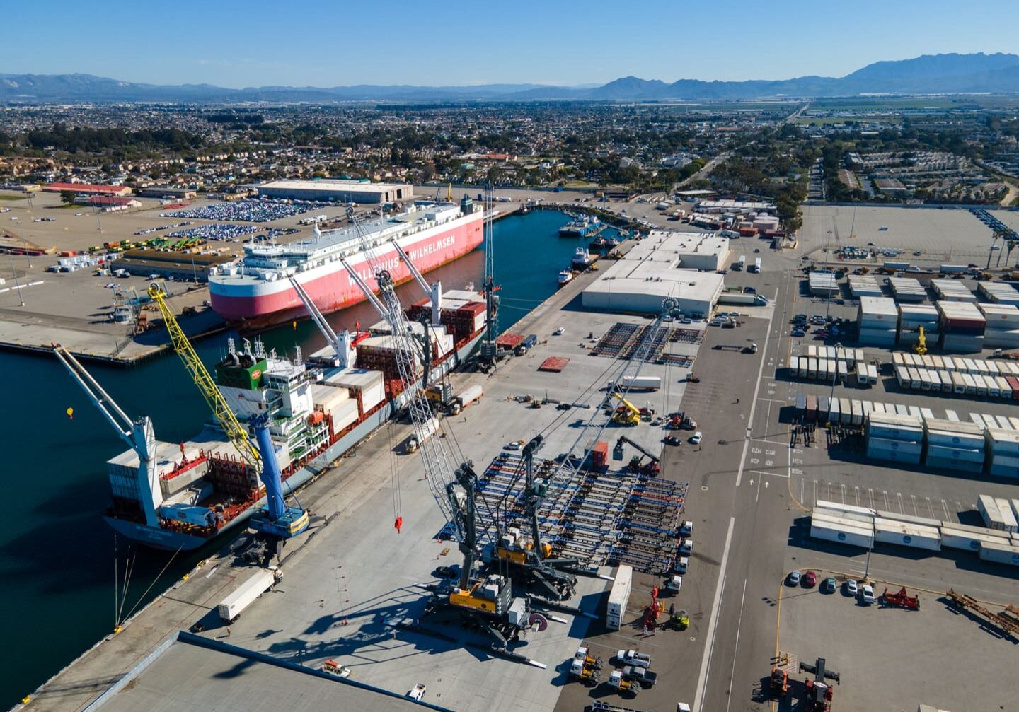 Aerial view of a working dock within the port focused on a red and white cargo ship.