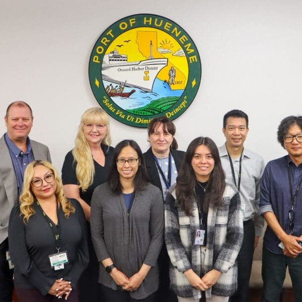 Eight people stand in front of a wall with the Port of Hueneme logo, celebrating a $3.935 million state grant as the Governor ramps up the California Port Data Partnership Program.