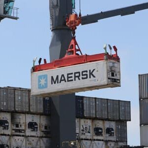 A shipping container labeled "Maersk" is strategically lifted by a crane at a busy port, showcasing logistical advantages. Other containers are stacked in the background.