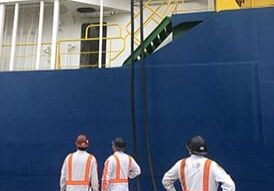 Three workers in safety gear observe a hose being hoisted onto a ship during the 2021 Dock Talk event.